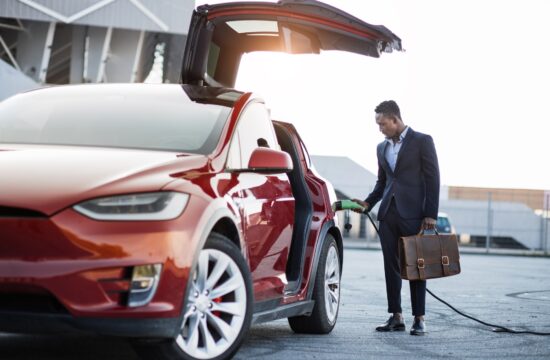 African businessman with suitcase charging electric car
