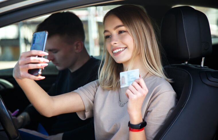 Happy smiling girl takes a selfie with a new drivers license, sitting next to an instructor
